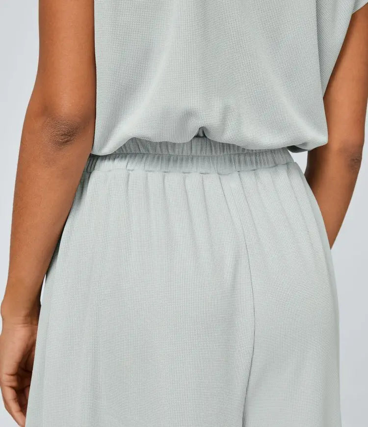 Neformální overal s V-výstřihem, širokými plisovanými nohavicemi, krátkým rukávem, boční kapsou a splývavou texturou